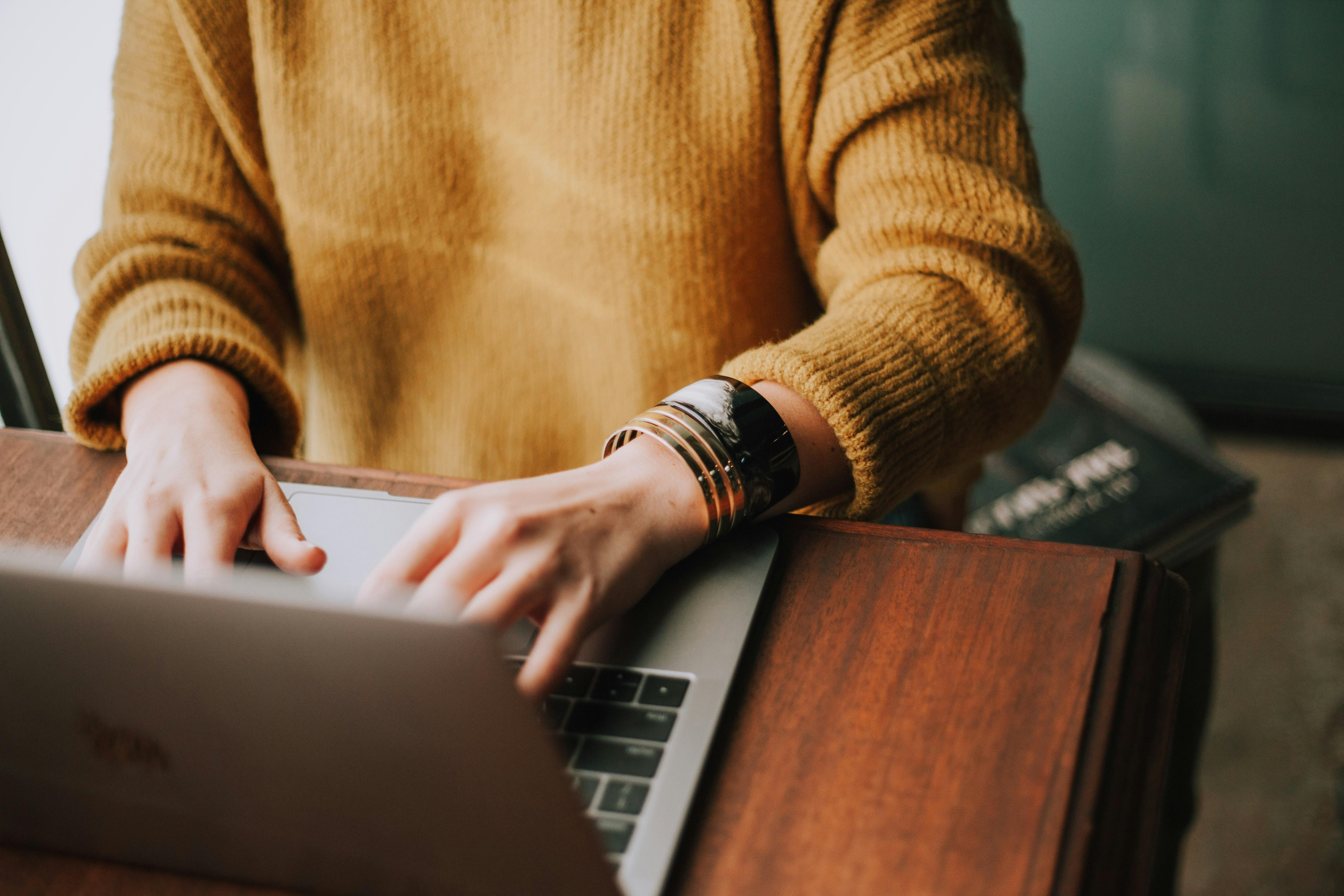 woman typing on computer in yellow sweater